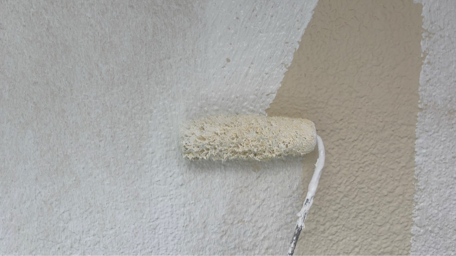 草加市の外壁塗装現場にて、ローラーを使用して白い下塗り材(フィラー)を丁寧に塗布している職人の作業風景