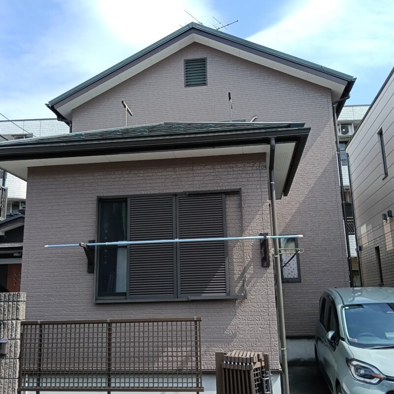 落ち着いたブラウン系のサイディング外壁と黒いサッシが調和した、2階建て住宅の外観。手前には駐車スペースとフェンスが見える。