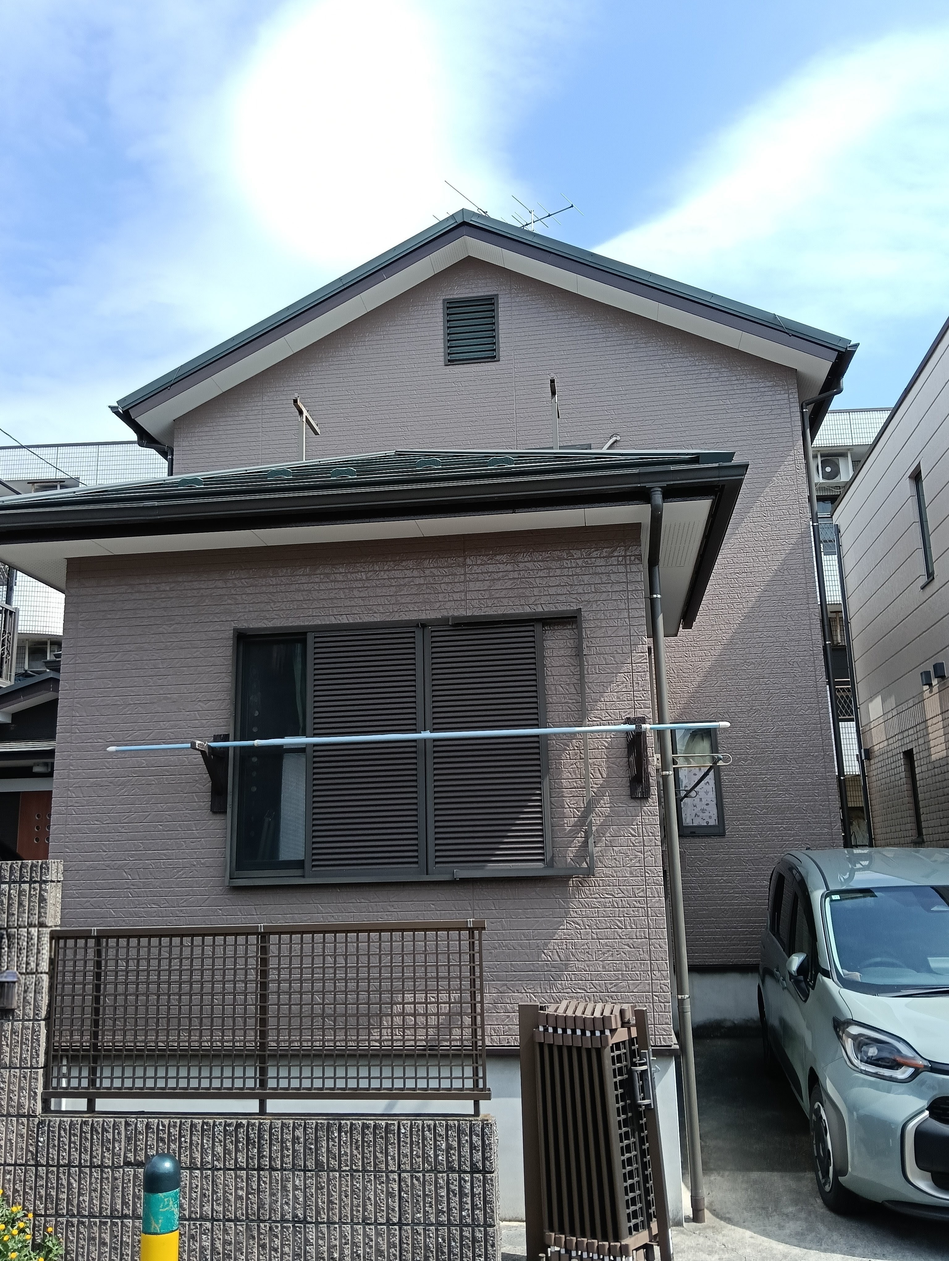 落ち着いたブラウン系のサイディング外壁と黒いサッシが調和した、2階建て住宅の外観。手前には駐車スペースとフェンスが見える。