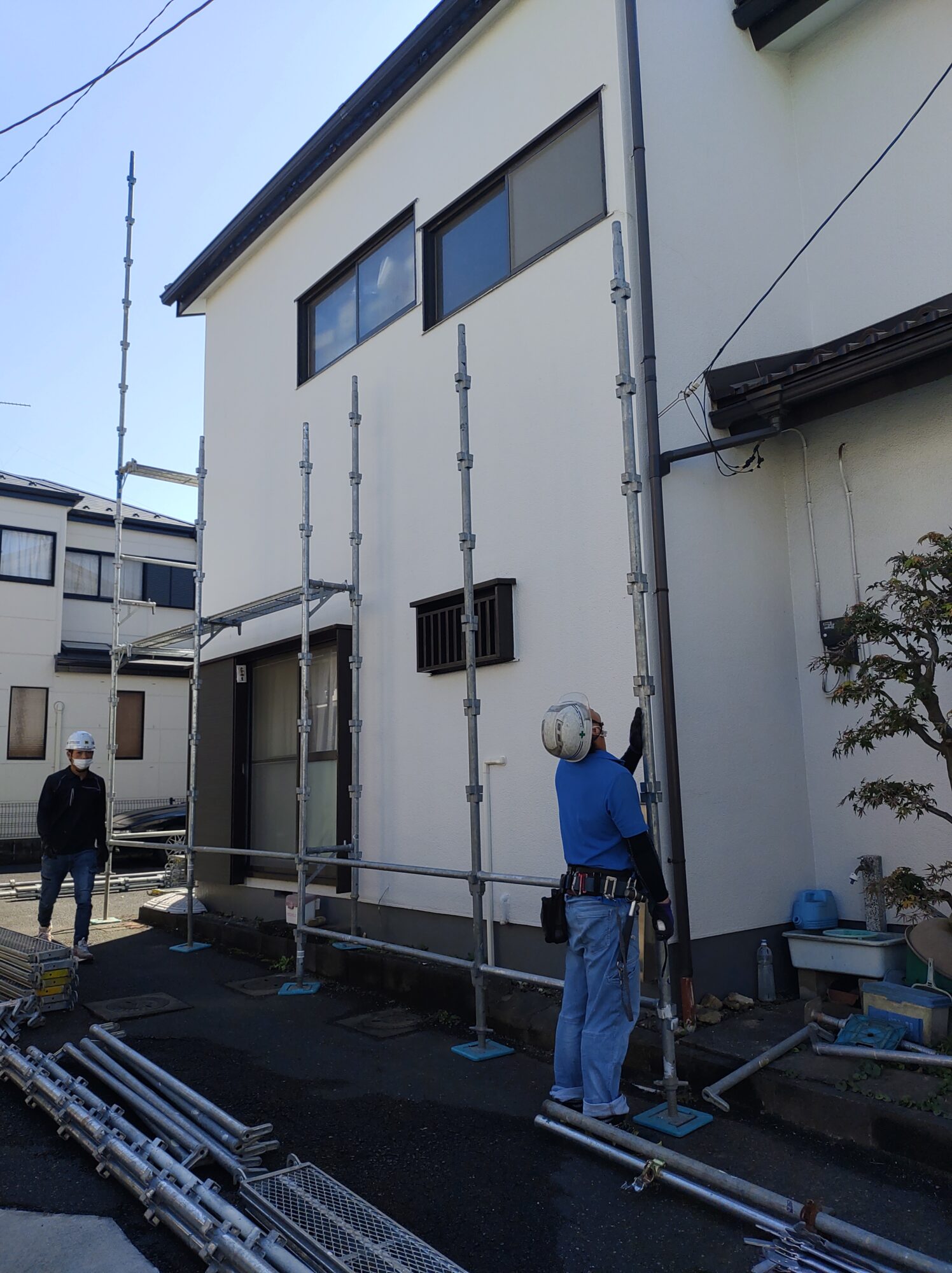 塗装工事が完了し、美しい艶と細かな凹凸模様が均一に仕上がった白いモルタル外壁。足場から建物の側面を見通したアングル。