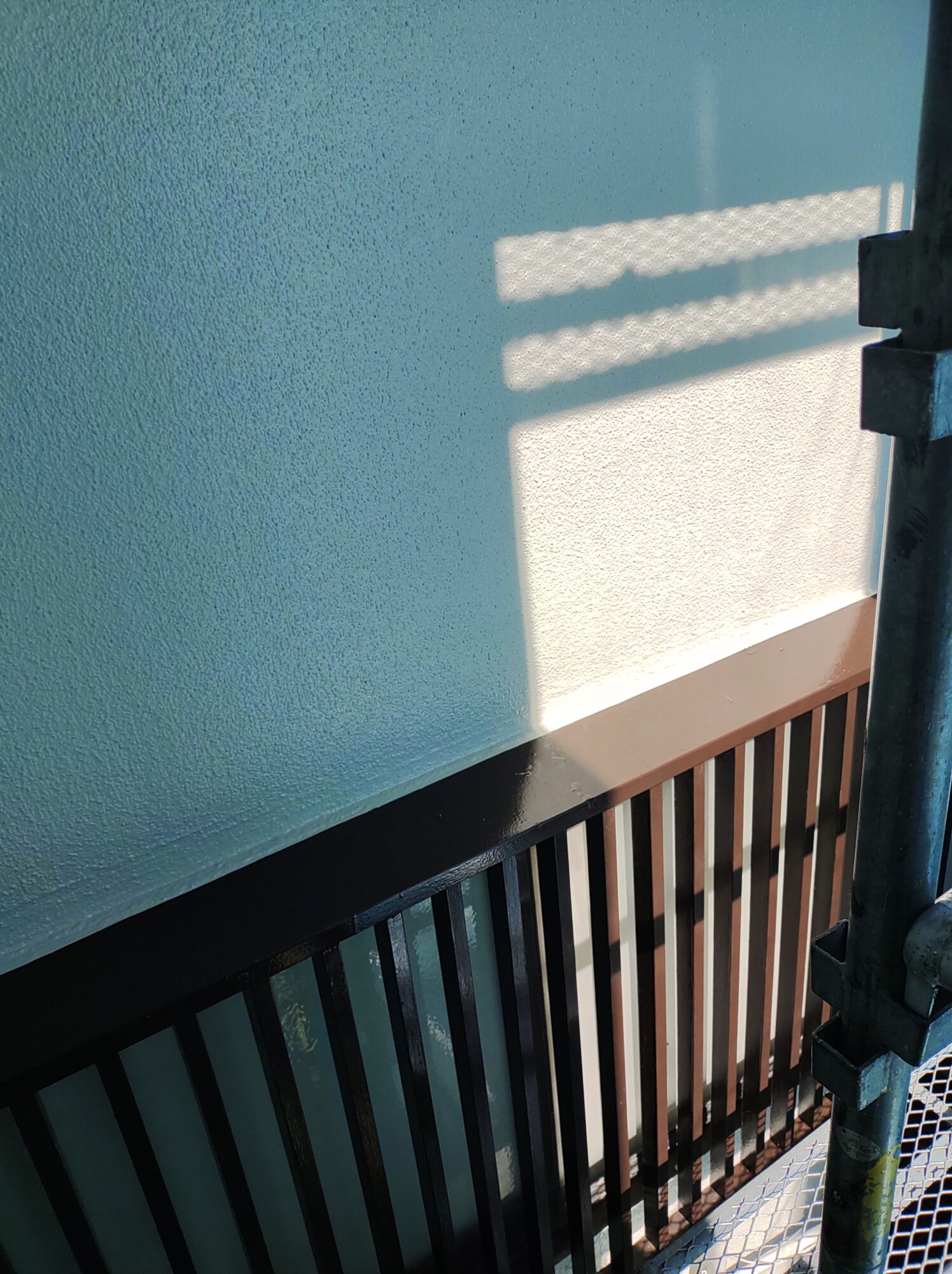 塗装工事が完了し、美しい艶と細かな凹凸模様が均一に仕上がった白いモルタル外壁。足場から建物の側面を見通したアングル。