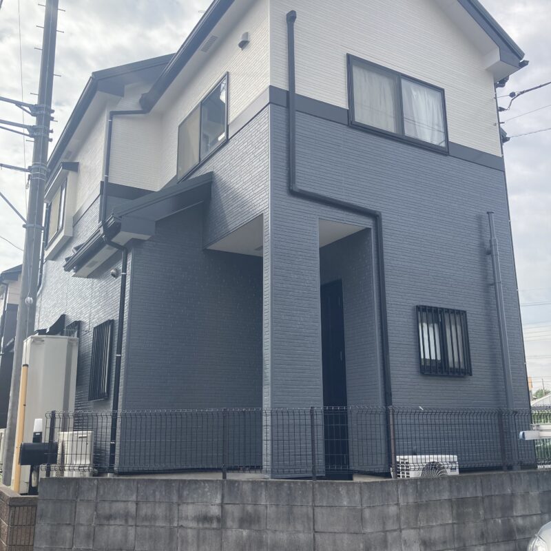 三郷市での外壁塗装・屋根カバー工法施工後の戸建て外観写真。1階部分にシックなチャコールブルーグレー、2階部分に明るいホワイトを配したツートンカラーで美しく塗り替えられ、雨樋や破風板などの付帯部もきれいに仕上げられたモダンな住宅。