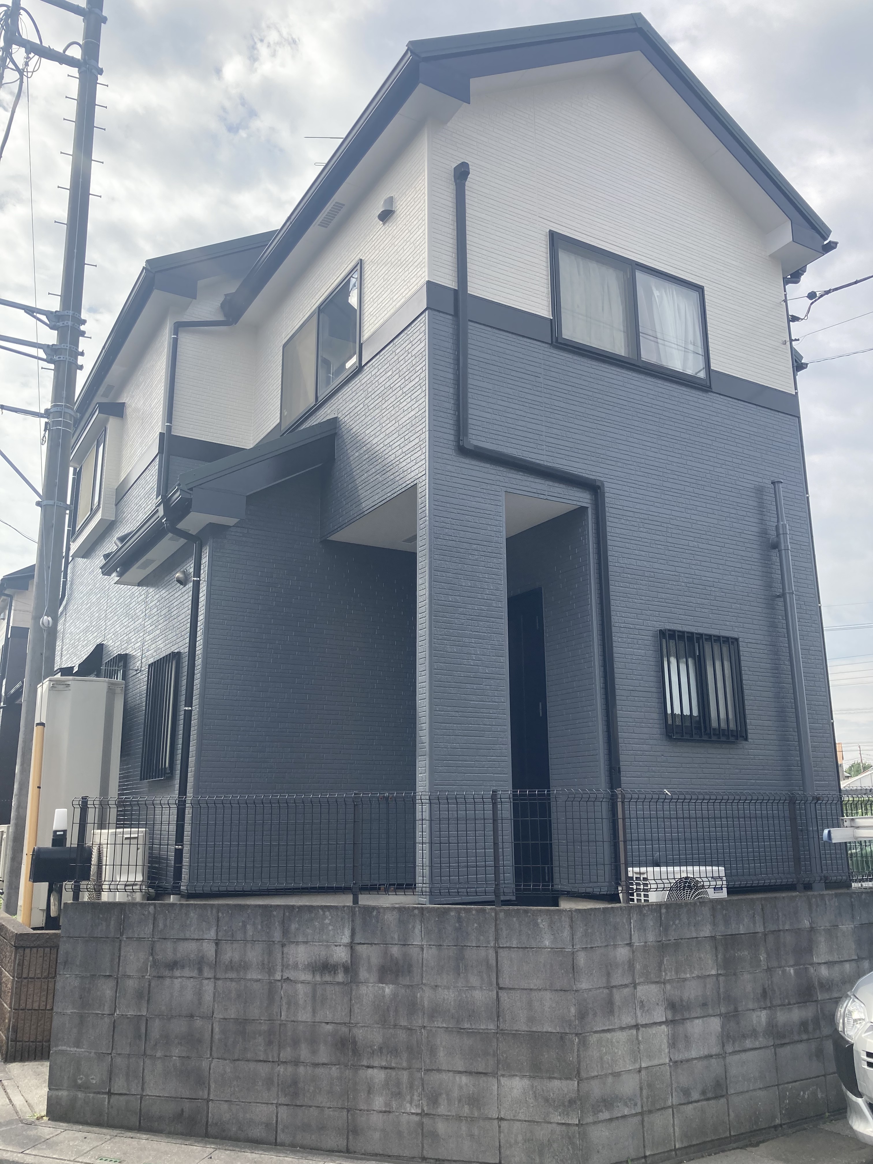 三郷市での外壁塗装・屋根カバー工法施工後の戸建て外観写真。1階部分にシックなチャコールブルーグレー、2階部分に明るいホワイトを配したツートンカラーで美しく塗り替えられ、雨樋や破風板などの付帯部もきれいに仕上げられたモダンな住宅。