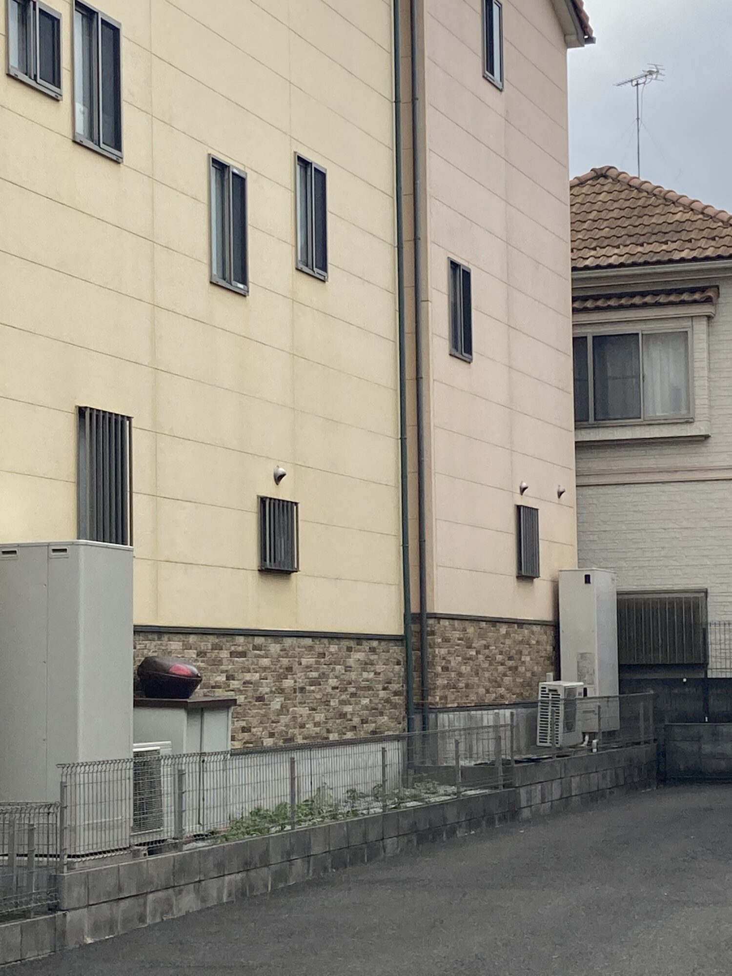 草加市のお住まいの外壁現地調査にて、経年劣化による色褪せや窓サッシ・排気口周辺からの雨だれ黒ずみ汚れが見られる、足場仮設前の縦に長い構造の建物外観写真