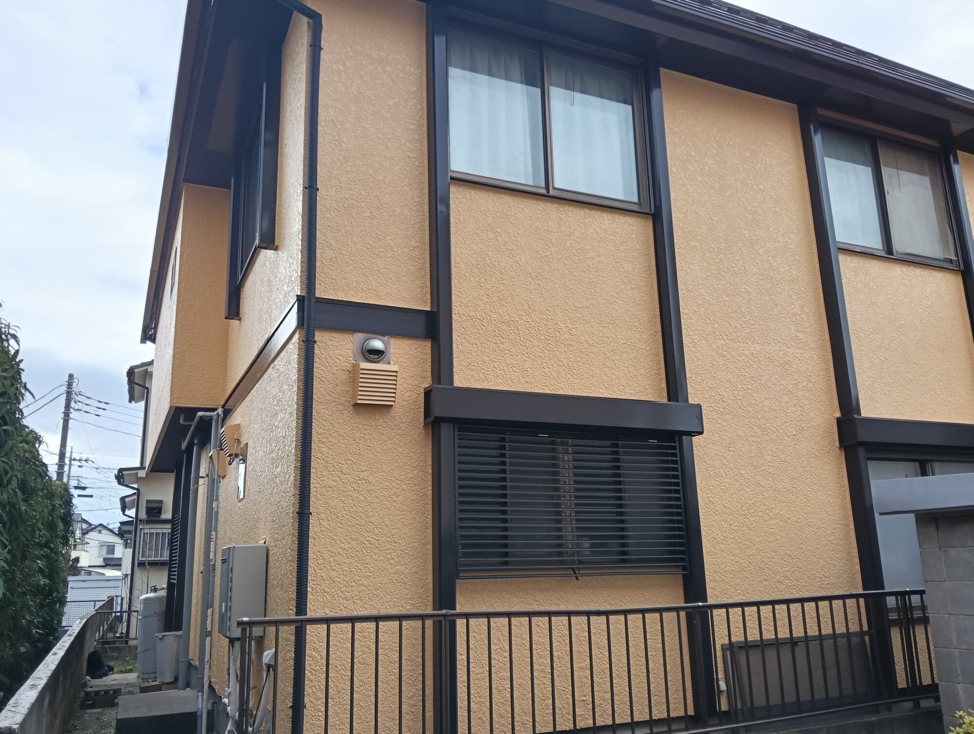 草加市の戸建て住宅にて外壁塗装工事がすべて完了し、足場撤去後にイエロー・ベージュ系の外壁とブラウンの附帯部が美しく調和したお住まいの引き渡し直前の外観写真