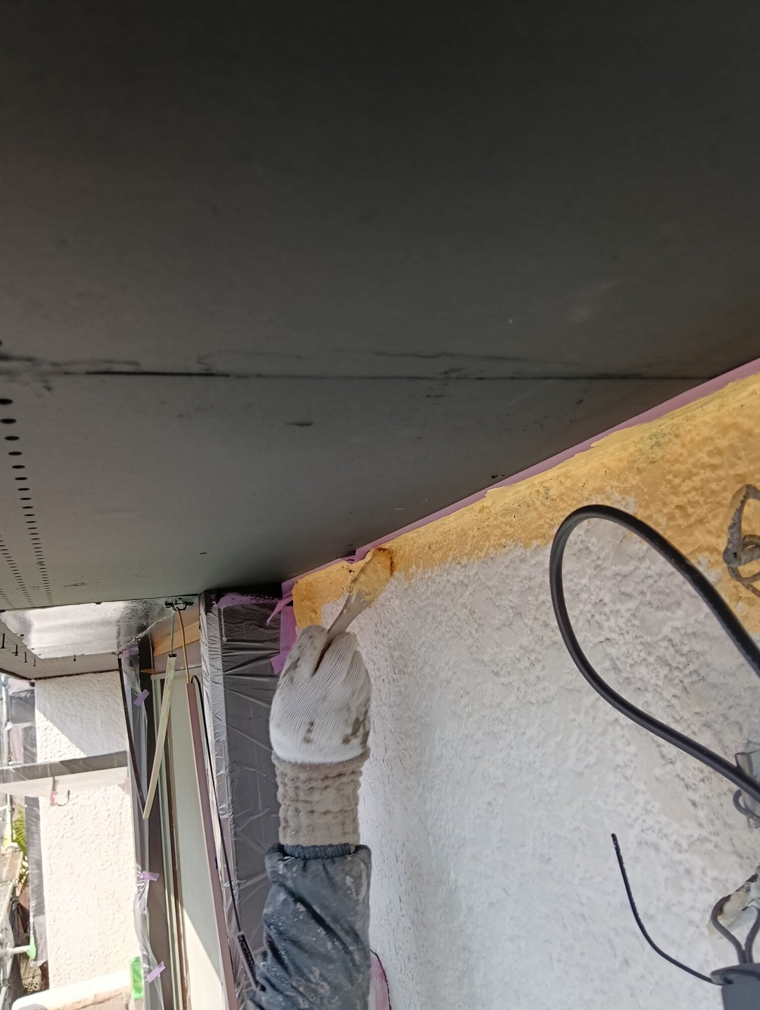 草加市の戸建て住宅における外壁塗装工事(中塗り工程)にて、職人が窓サッシのキワや細かい隙間を刷毛(はけ)を使って丁寧にダメ込みしている様子