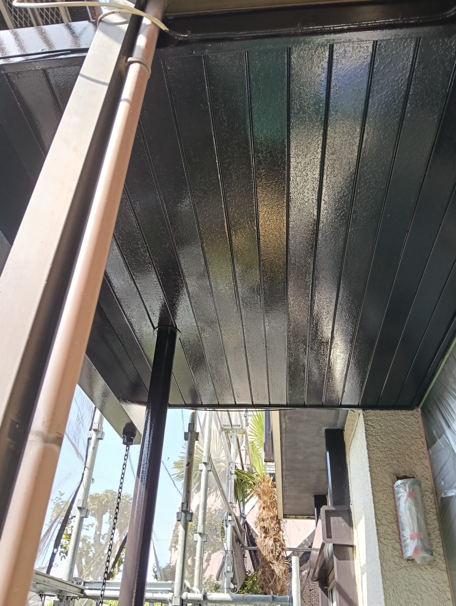 草加市の戸建て住宅のベランダにて、職人が刷毛を使って鉄製の手すりに仕上げの上塗り塗料（グレー）を丁寧に塗布し、美しいツヤを出している様子