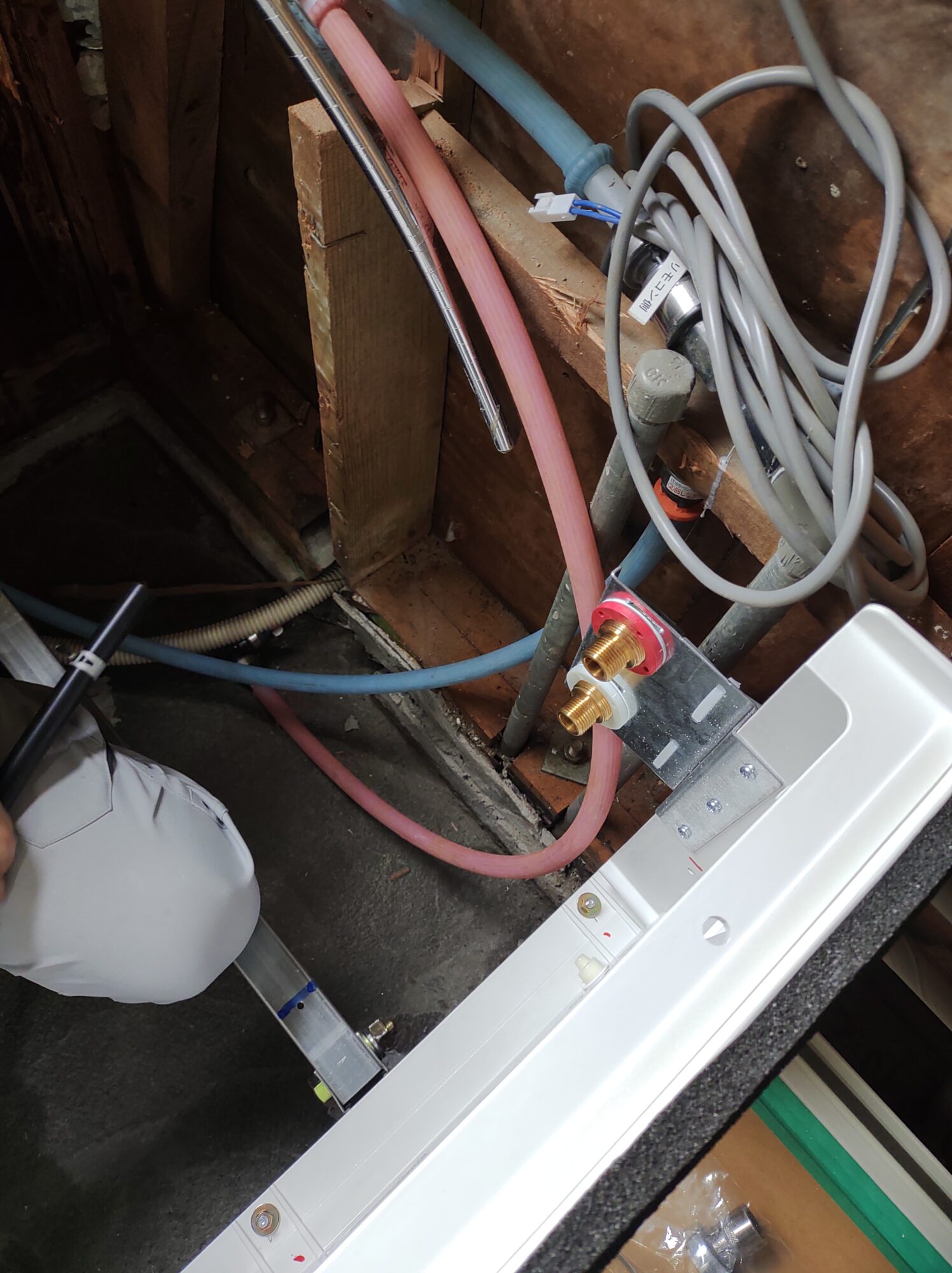 草加市のお風呂リフォーム現場にて、新設したユニットバス床パネルの裏側で、架橋ポリエチレン管の給水管(青)と給湯管(ピンク)を水栓接続金具へ確実に結びつけている床下設備配管工事の写真