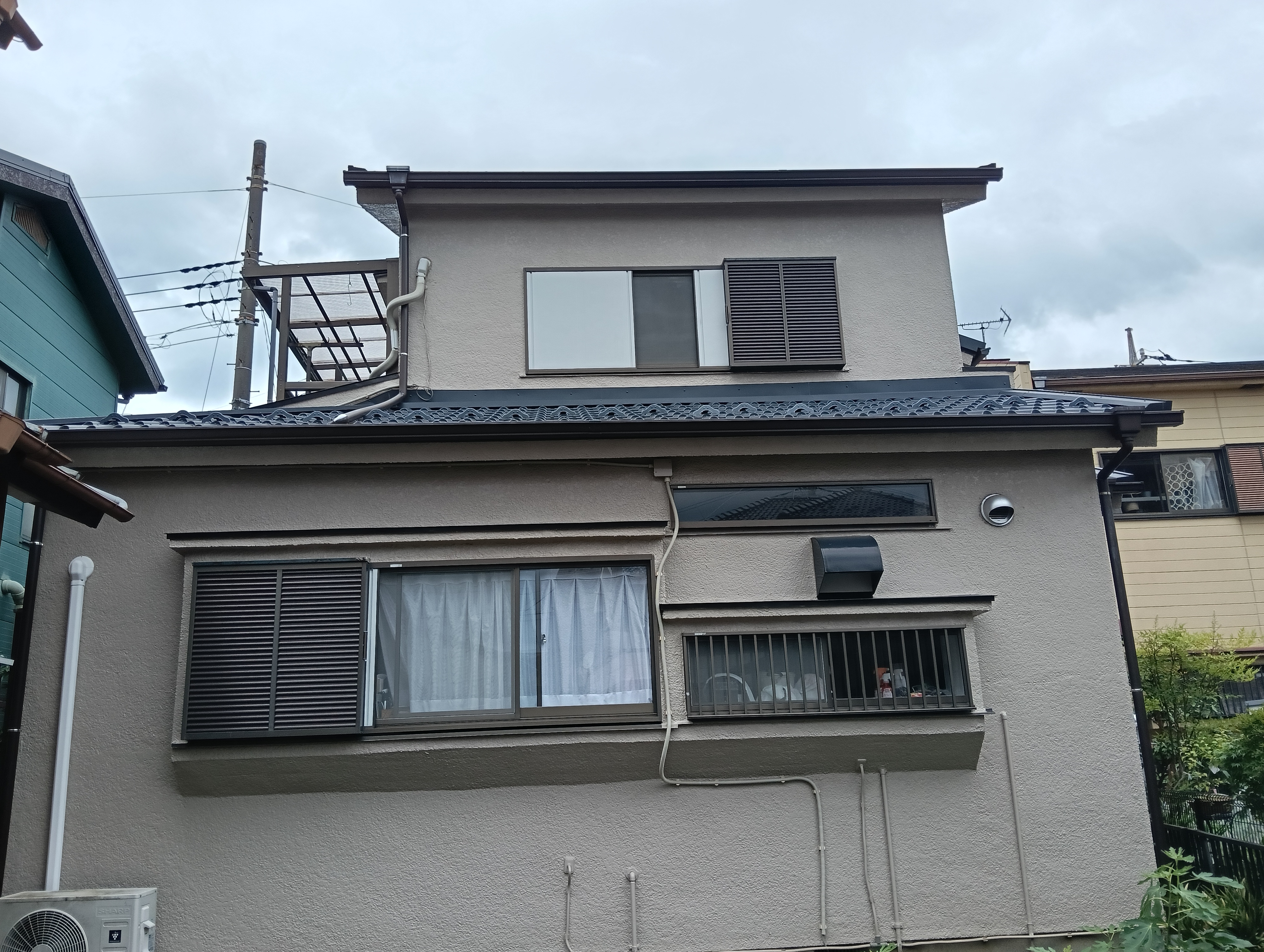 草加市のお住まいで古い日本瓦から軽量な黒のガルバリウム鋼板への屋根葺き替え工事が美しく完工し、雨樋や板金付帯部も完璧に仕上がった戸建て住宅の外観全景写真