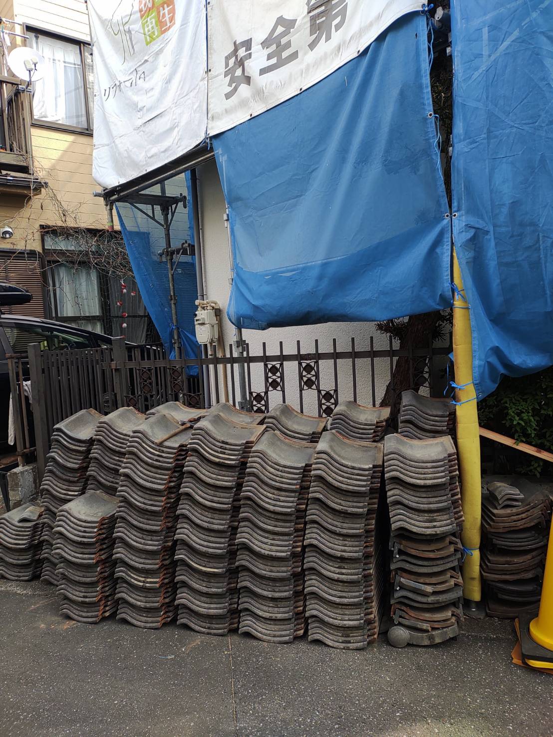 草加市の屋根葺き替えリフォーム現場にて、解体撤去された古い日本瓦が近隣配慮と安全確保のために敷地内へ美しく整然と積み上げられた地上施工写真