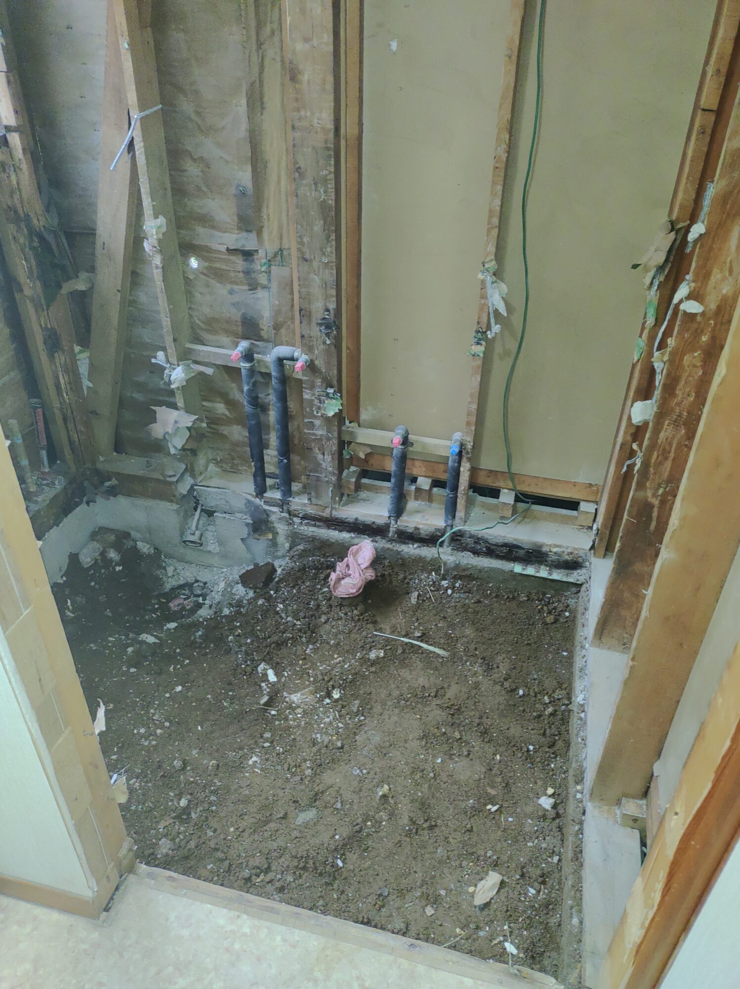 草加市の戸建て浴室リフォーム現場にて、古いタイル貼りお風呂を完全解体し、木部の土台や柱を露出させて新しい給水管・給湯管を立ち上げたユニットバス仮設前の床下・壁裏構造写真