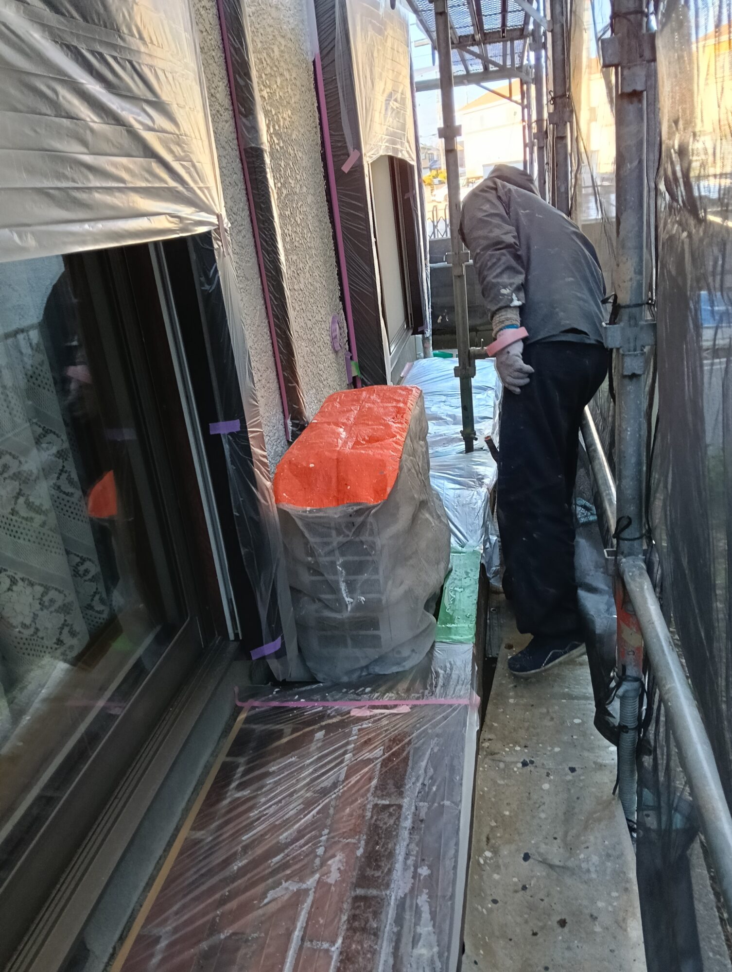 草加市の戸建て外壁塗装工事にて、窓サッシまわりを汚さないようビニールとマスキングテープを使って職人がシワなく綺麗に養生している様子