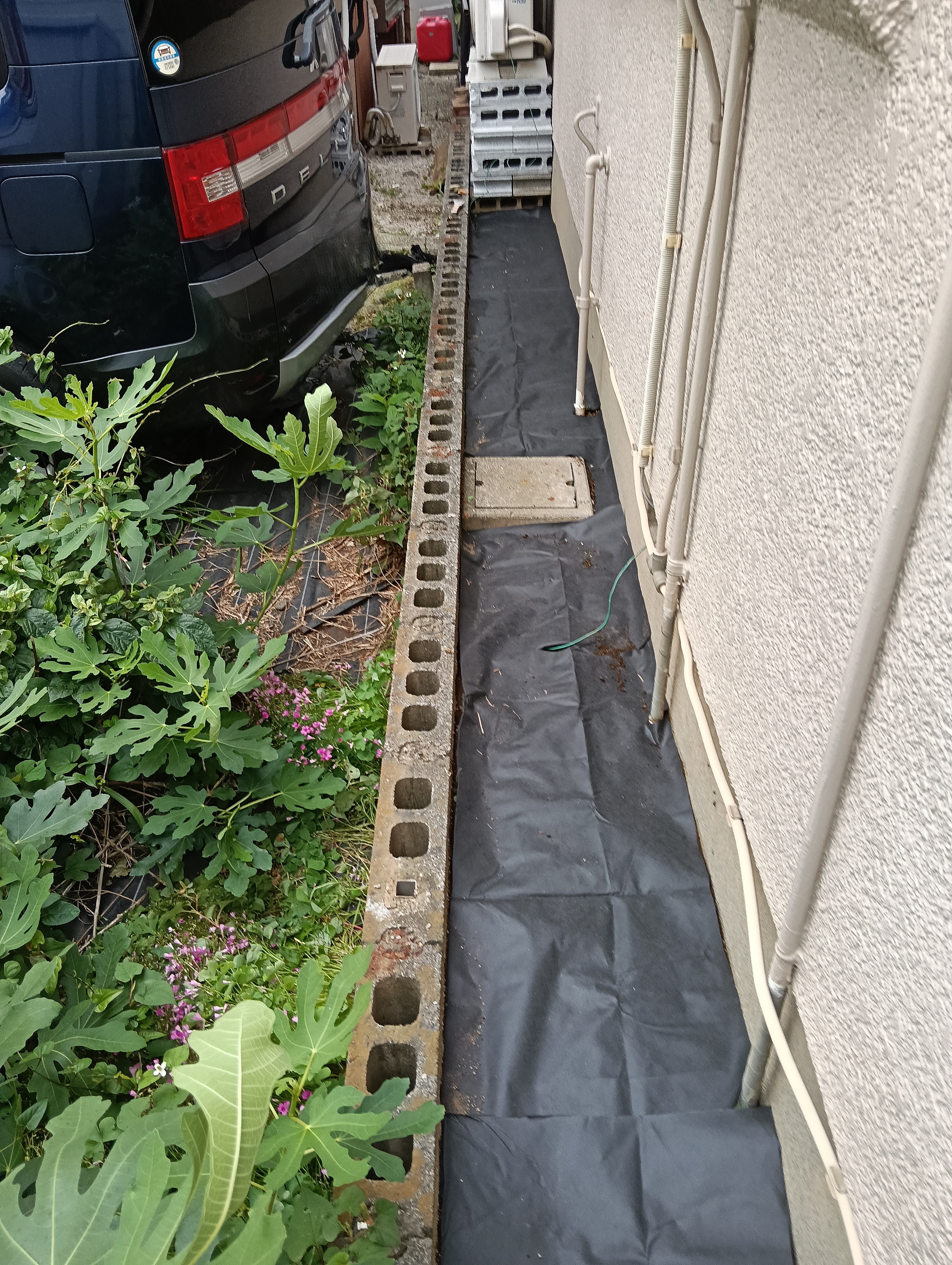 草加市の外構フェンス入替工事現場にて、雑草対策として建物と既存ブロック塀の間の狭い犬走り通路へ隙間なく防草シートを敷設した施工中写真
