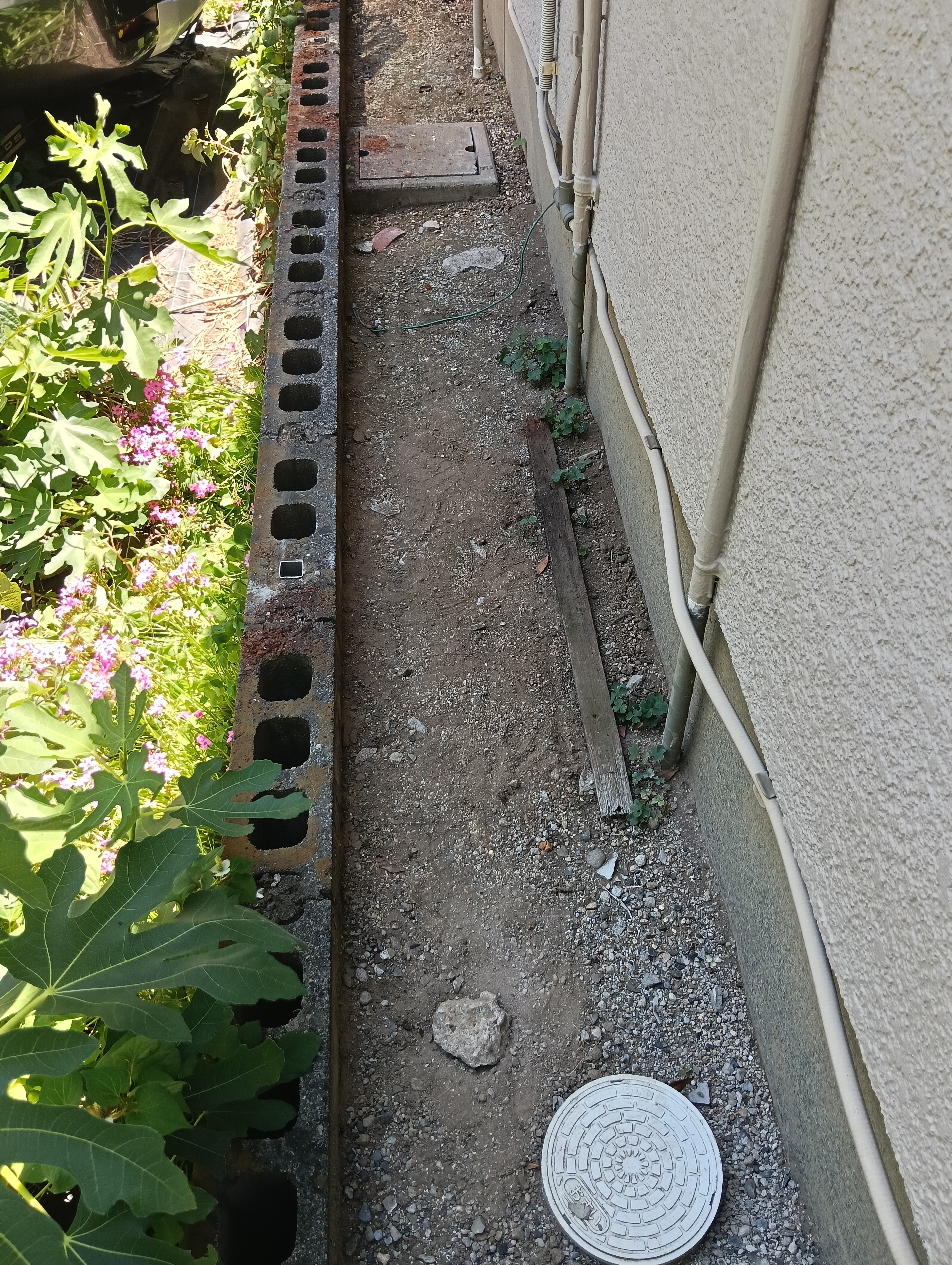 草加市の外構フェンス入替工事にて、古い金属フェンスと支柱をきれいに取り外し、既存のブロック塀の天端に新しい支柱を建てるための四角い柱穴が並んでいる施工中写真