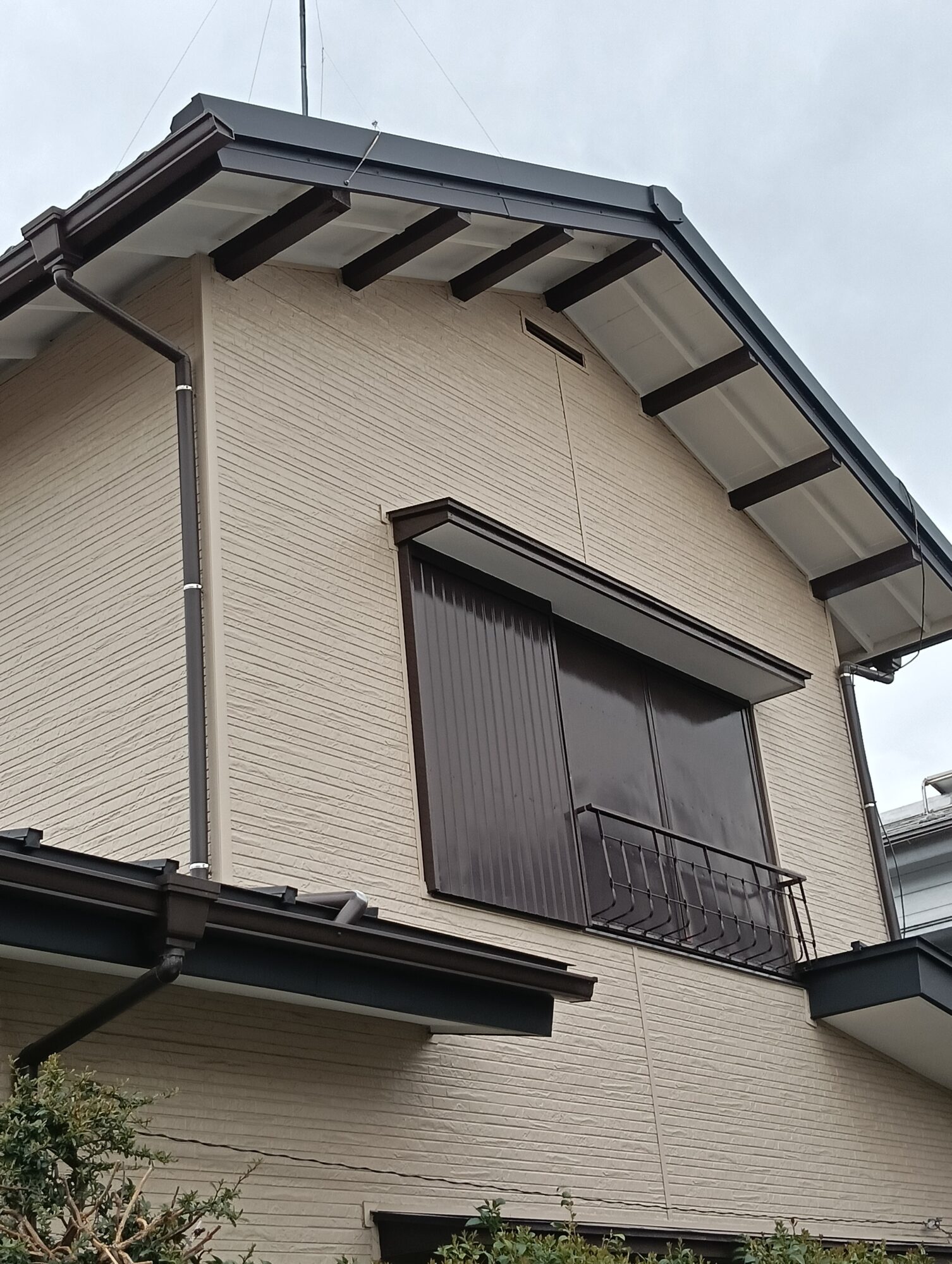 川口市での外壁リフォーム施工後。新しく張り替えたベージュ系の金属サイディングと、黒で美しく塗装・仕上げされた軒天や破風板、雨戸サッシまわりの外観クローズアップ。