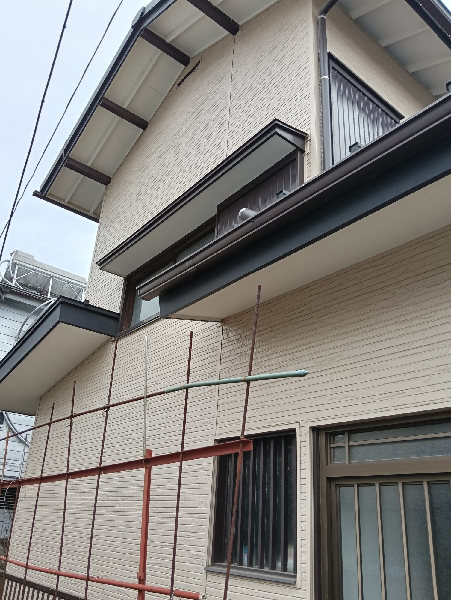 川口市での外壁リフォーム施工後。新しく張り替えたベージュ系の金属サイディングと、黒で美しく塗装・仕上げされた軒天や破風板、雨戸サッシまわりの外観クローズアップ。