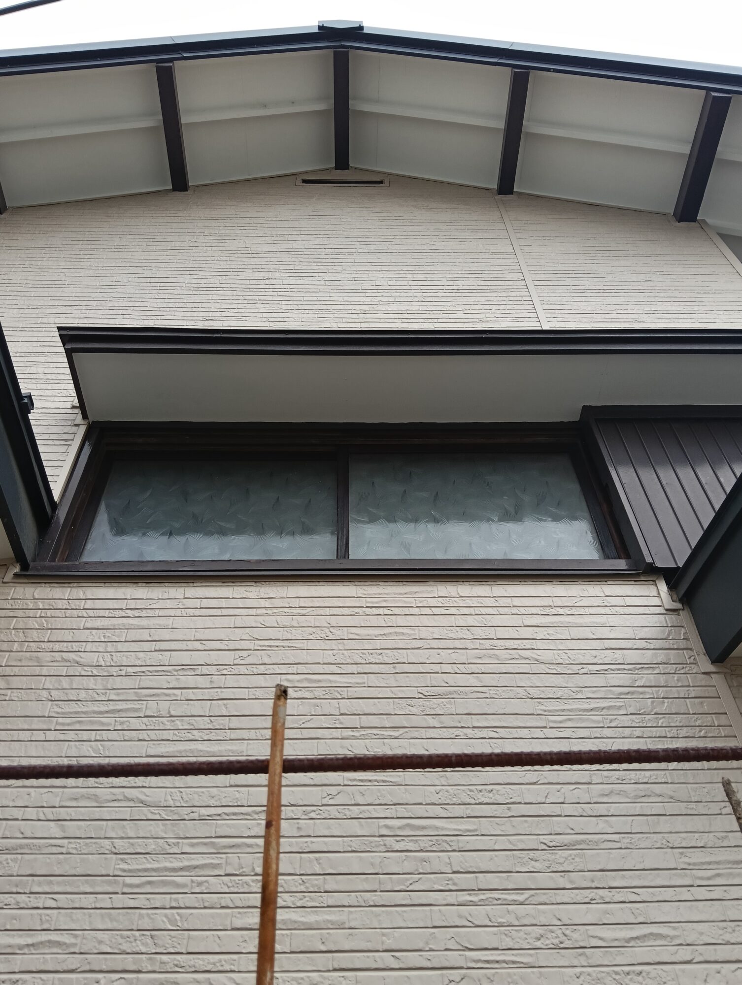 川口市での外壁リフォーム施工後。新しく張り替えたベージュ系の金属サイディングと、黒で美しく塗装・仕上げされた軒天や破風板、雨戸サッシまわりの外観クローズアップ。