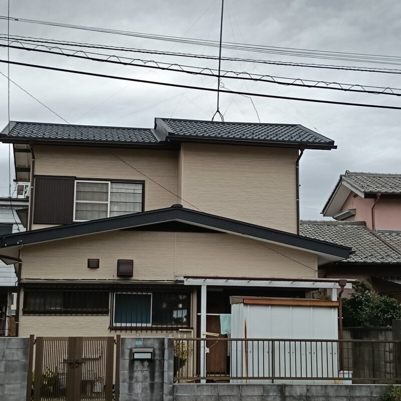 川口市の一戸建て外装リフォーム完了後の外観。外壁に施されたベージュの金属サイディングと、新しく葺き替えられた黒い瓦風の金属屋根が美しく調和した和モダンな住宅。