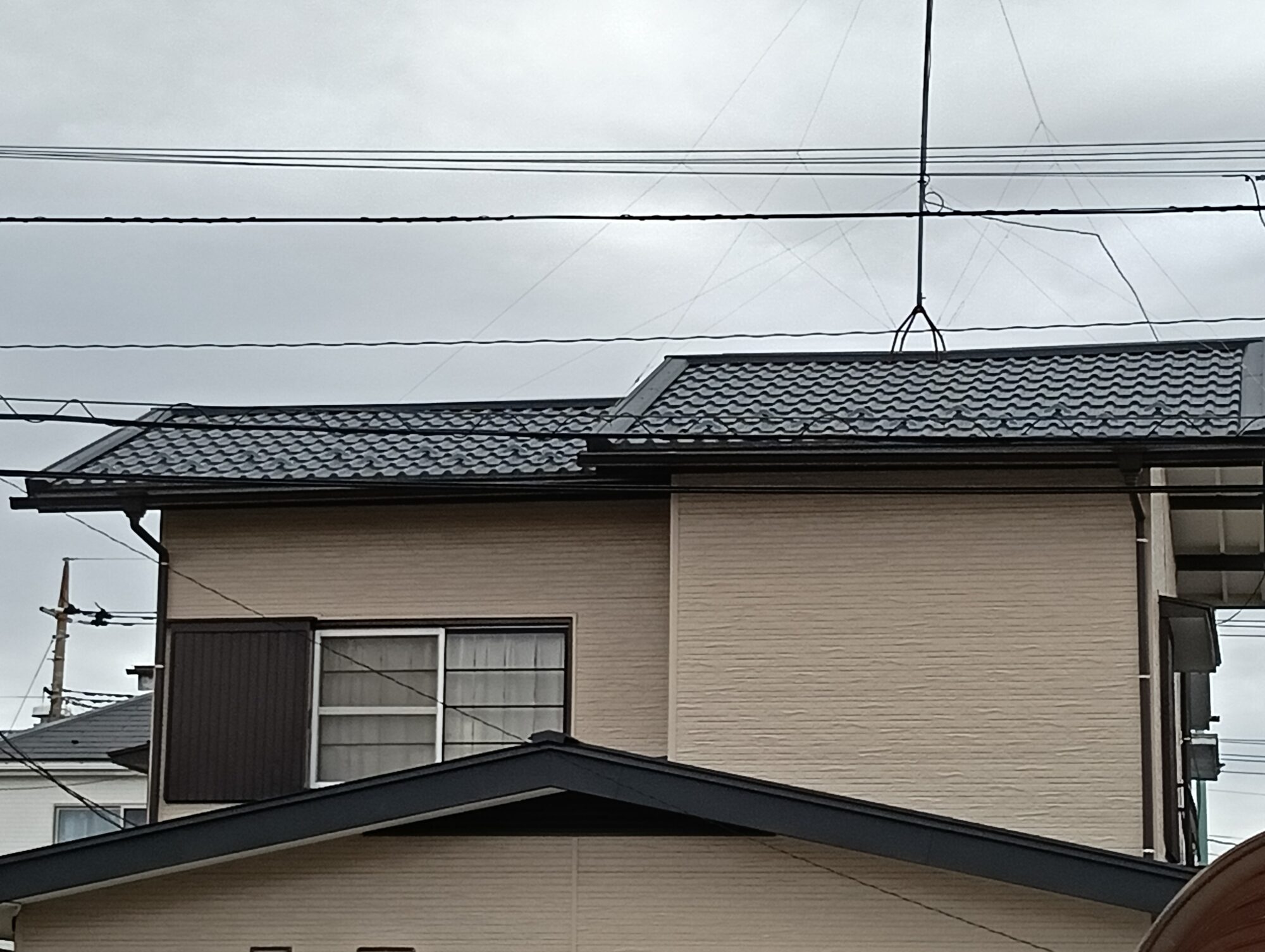 川口市での屋根葺き替え工事(またはカバー工法)の施工後。和風・洋風どちらの住宅にも馴染む、黒(ダークカラー)の和瓦風デザインの新しい金属屋根材が美しく仕上がった一戸建ての屋根外観。